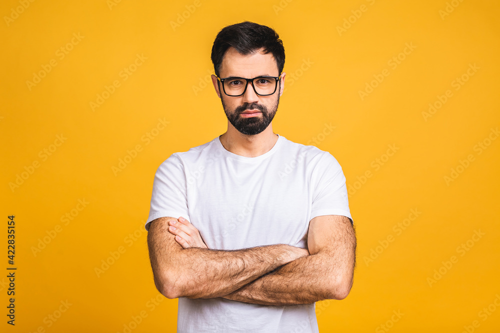 Serious man with crossed hands folded standing isolated on yellow background and looking at camera Serious man with crossed hands folded standing isolated on yellow background and looking at camera