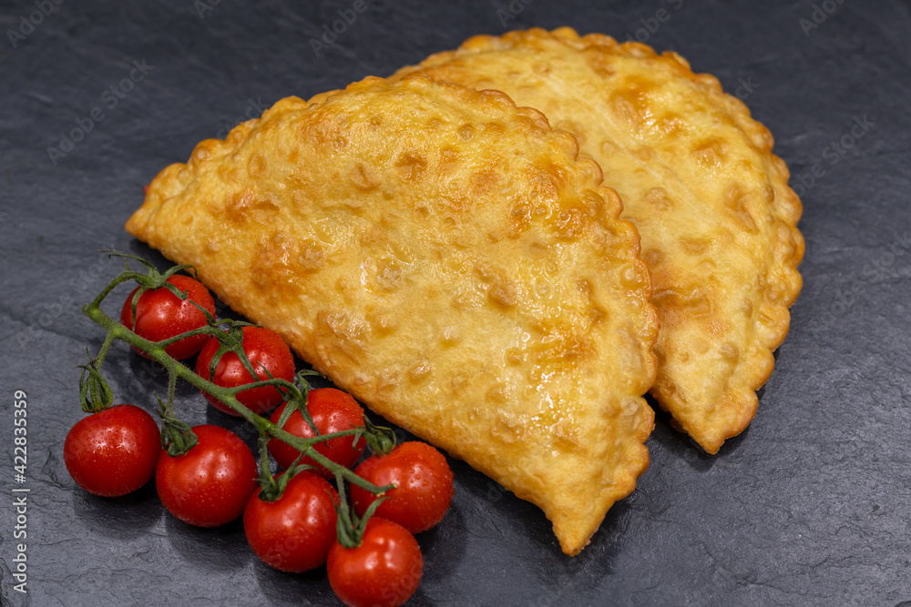 Chebureks on a black background. Served with cherry tomatoes. Caucasian cuisine. Chebureks on a black background. Served with cherry tomatoes. Caucasian cuisine.