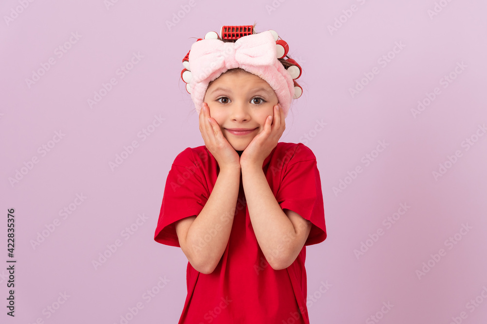A little girl holds her cheeks. Curling hair with curlers. A little girl holds her cheeks. Curling hair with curlers.