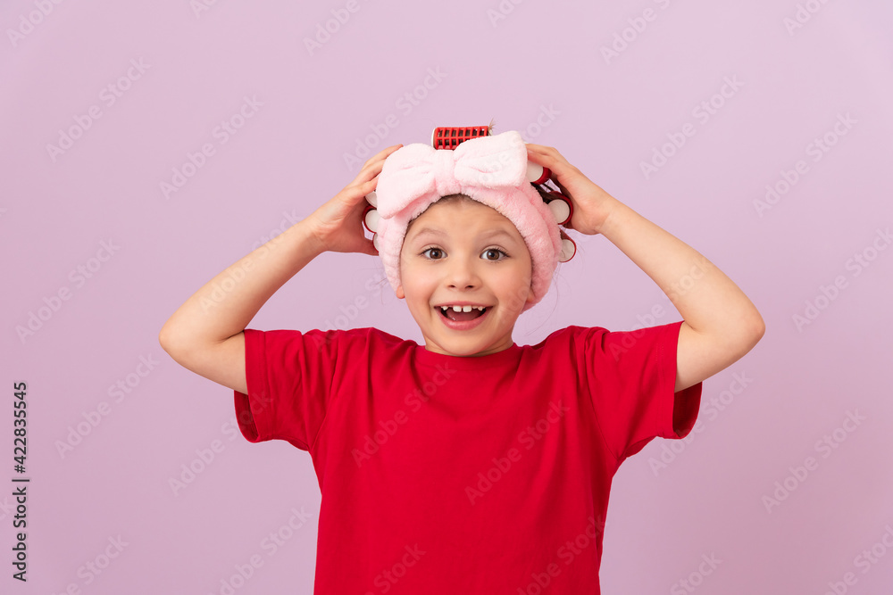 A little girl holds her cheeks. Curling hair with curlers. A little girl holds her cheeks. Curling hair with curlers.
