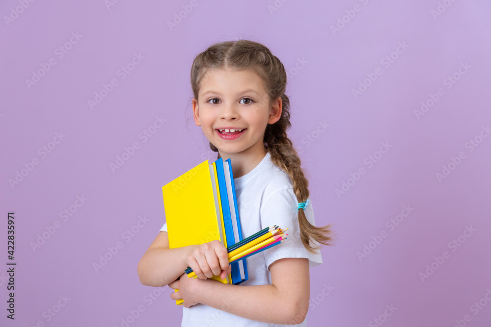 A little girl with pigtails on her head holds several books and pencils. A little girl with pigtails on her head holds several books and pencils.