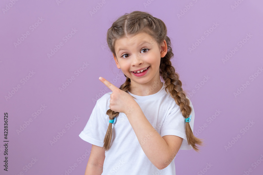 A little girl on an isolated background smiles and points her finger to the side. A little girl on an isolated background smiles and points her finger to the side.