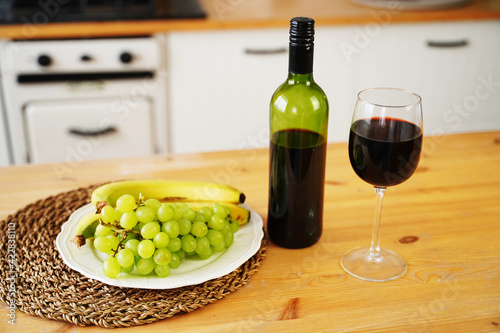 Close up of bottle and glass of red wine with berries and fruits on plate. Preparation on table for dating in kitchen.