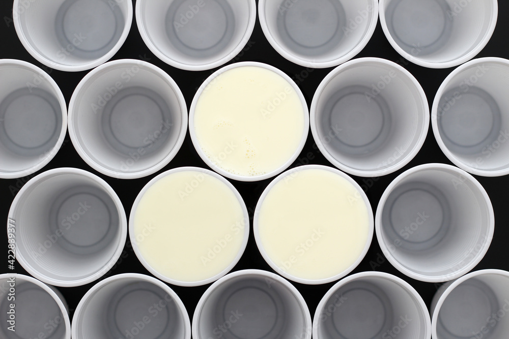 Many white plastic disposable cups, tree are filled with milk , view from above