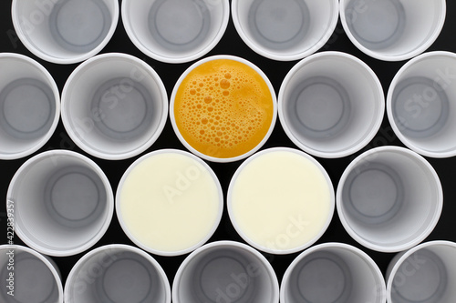 White plastic disposable cups filled with milk and orange juice, view from above