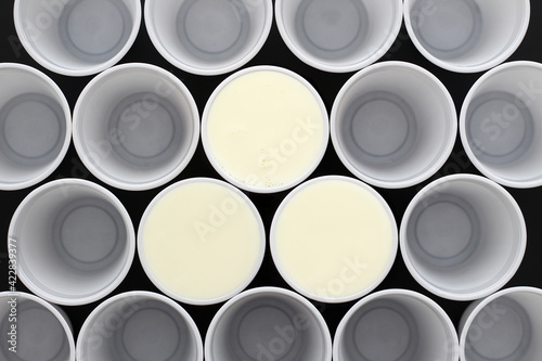 Many white plastic disposable cups, tree are filled with milk , view from above