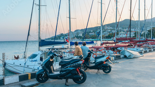 two young men arrived at the port embankment on motorcycles. Young people relax in the port and look at the moored yachts