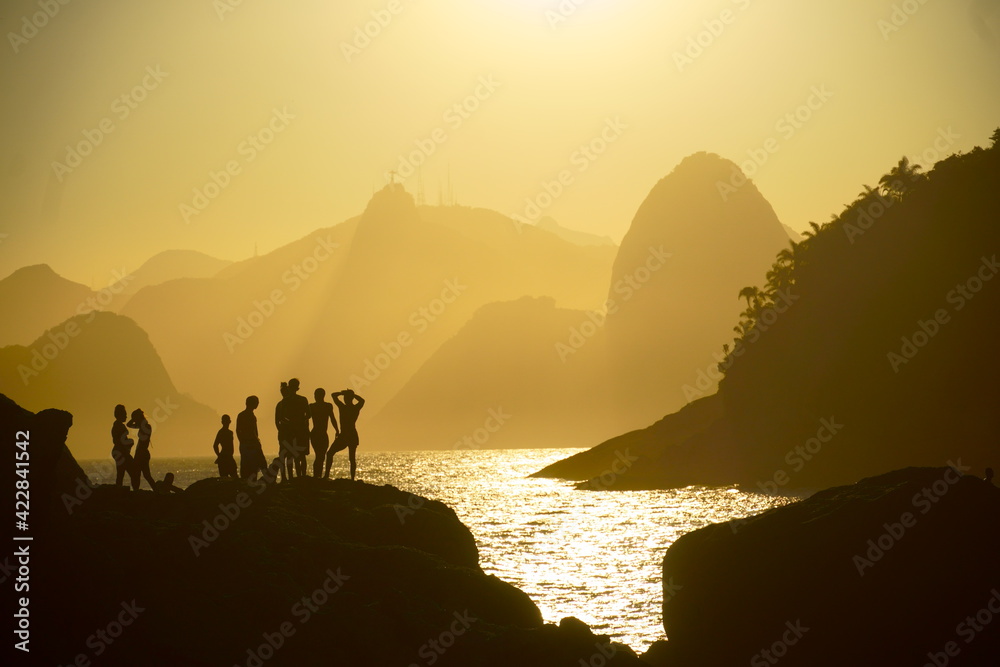 beautiful sunset at Piratininga beach, Niterói, overlooking the hills of Rio de Janeiro. Silhouette of some people on top of the rocks. Sunny summer day.