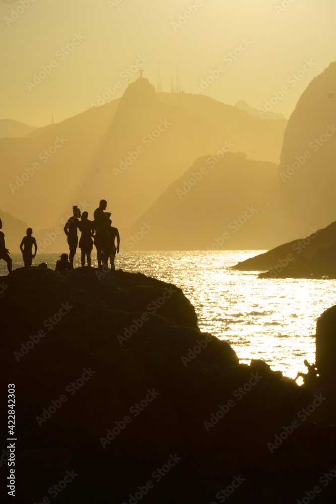 beautiful sunset at Piratininga beach, Niterói, overlooking the hills of Rio de Janeiro. Silhouette of some people on top of the rocks. Sunny summer day.