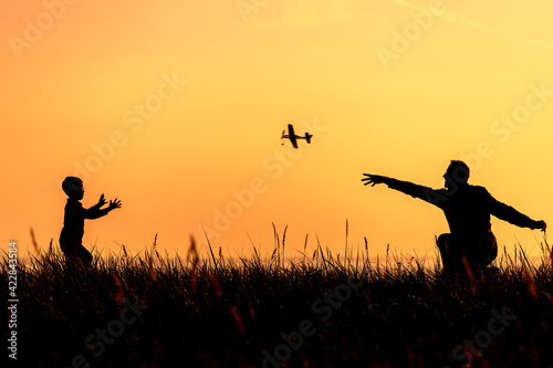 Silhouettes of a father and a little son playing with a toy plane at sunset background.
