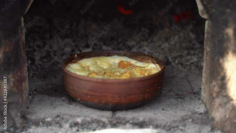 Clay pot with simmering porridge stands in old Russian stove made from bricks. Firewood crackles and gives heat