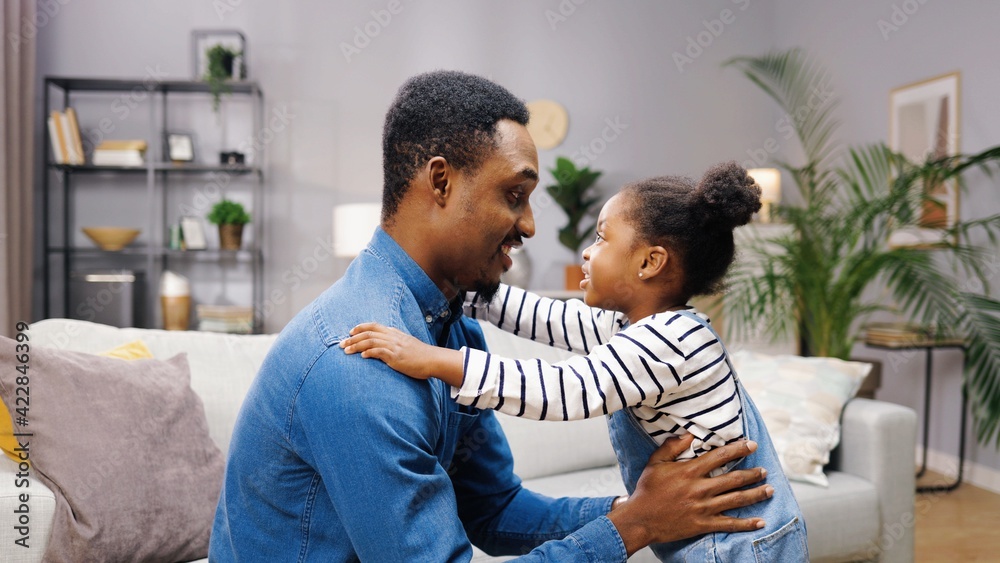 Happy young African American father hugs his cute little daughter tightly. Parental love and care. Carefree childhood. Happy young African American father hugs his cute little daughter tightly. Parental love and care. Carefree childhood.