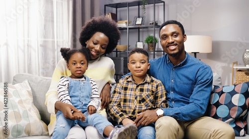 African American family with kids sitting on sofa in room, looking at camera and smiling, positive emotions, parents with children gathered together at home parenting concept