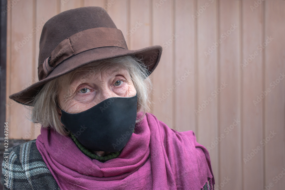 Happy older woman in a black protective mask against coronavirus infection. COVID-2019 quarantine. Senior Health. Threat to the life of the elderly coronavirus. Fashionable grandmother in a hat Happy older woman in a black protective mask against coronavirus infection. COVID-2019 quarantine. Senior Health. Threat to the life of the elderly coronavirus. Fashionable grandmother in a hat
