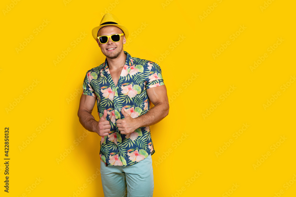 Young sportve man on vacation wearing floral summer shirt over yellow background success sign doing positive gesture with hand, thumbs up smiling and happy. Cheerful expression and winner