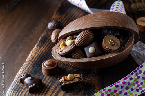 A close up of a chocolate Easter egg filled with gourmet chocolates on a wooden board.