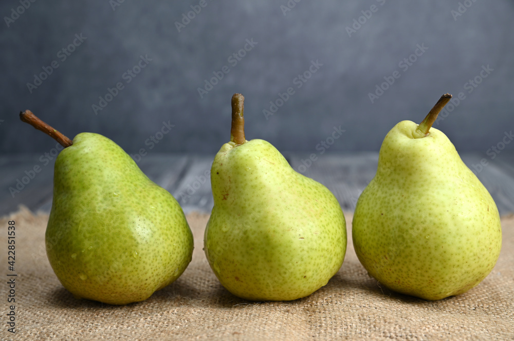 Three green pears of the same sort are standing next to each other on sackcloth Three green pears of the same sort are standing next to each other on sackcloth