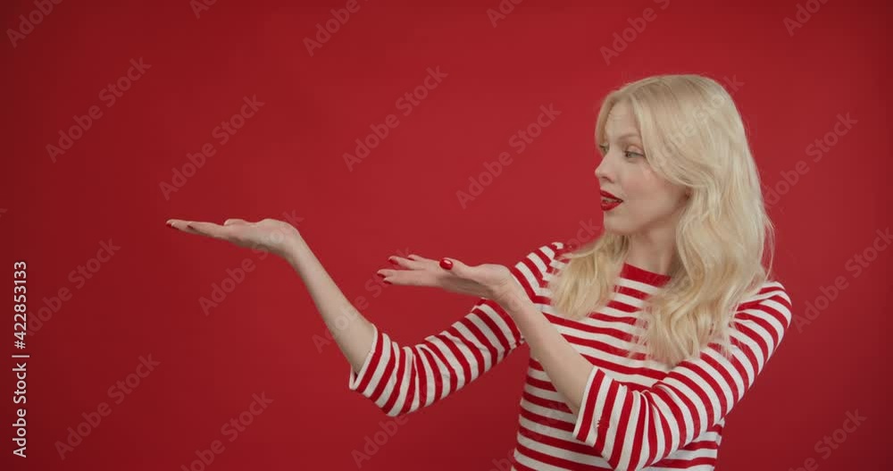 Happy woman presenting product. Portrait of female customer showing empty place on red background. Young blonde woman advertising service in studio. Female model present copy space