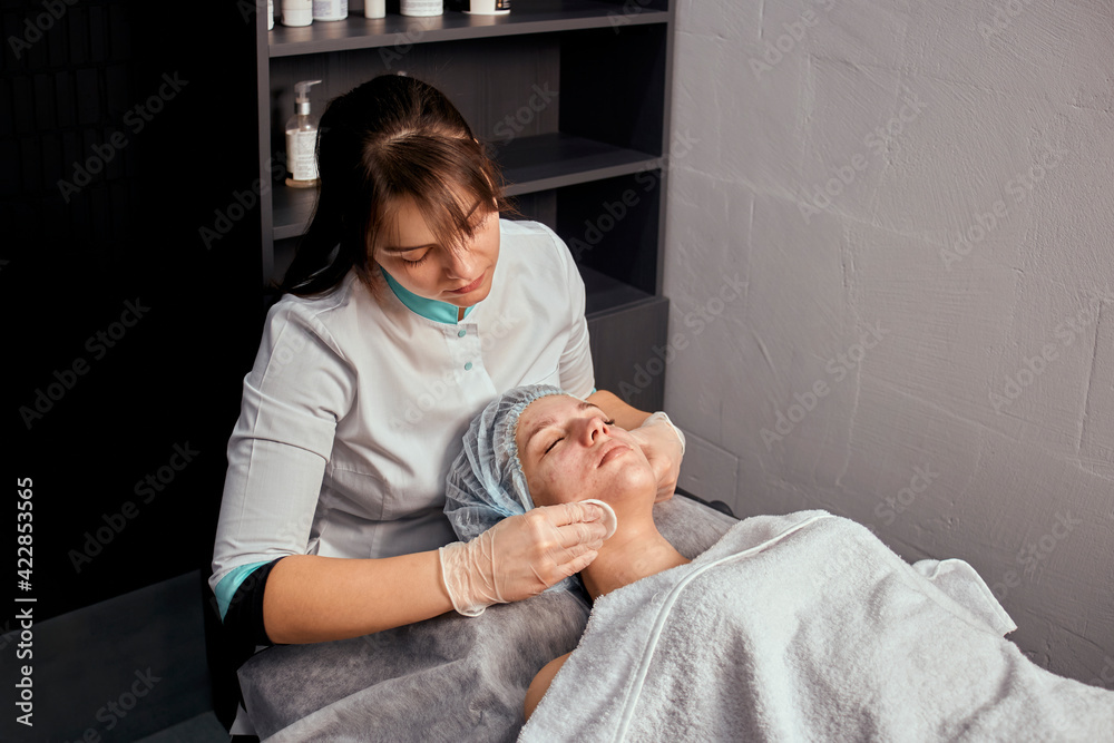 Obraz premium Professional facial skin care in a beauty salon. Mechanical cleaning of the face with cotton pads. Cleansing the face of a young female client.