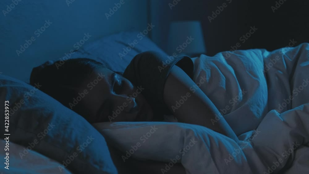 Trouble sleeping. Night insomnia. Bedtime fatigue. Disturbed tired woman lying in bed with closed eyes late in dark home bedroom with blue light.