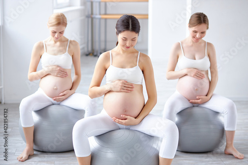 Pregnant women sitting on fitball and touching belly