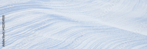 Beautiful winter background with snowy ground. Natural snow texture. Wind sculpted patterns on snow surface. Wide panoramic texture for background and design. © Andrei Stepanov