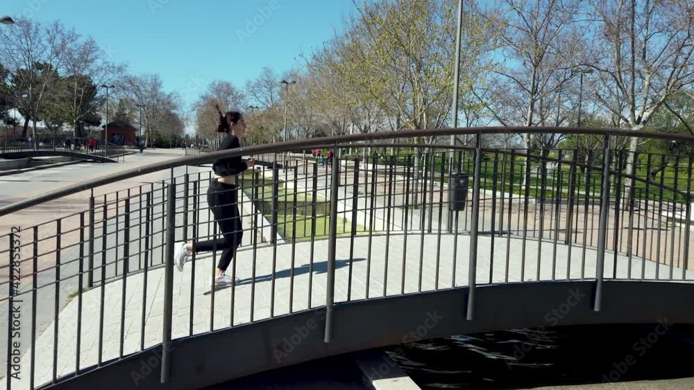 teenage girl running in a park dressed in black over a bridge with trees in the background. slow motion video teenage girl running in a park dressed in black over a bridge with trees in the background. slow motion video
