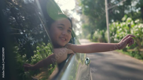 Happy Asian family enjoy and having fun together with outdoor lifestyle activity on road trip vacation. Little child girl kid sit in the car with pull her face and hand out of car window in summer day