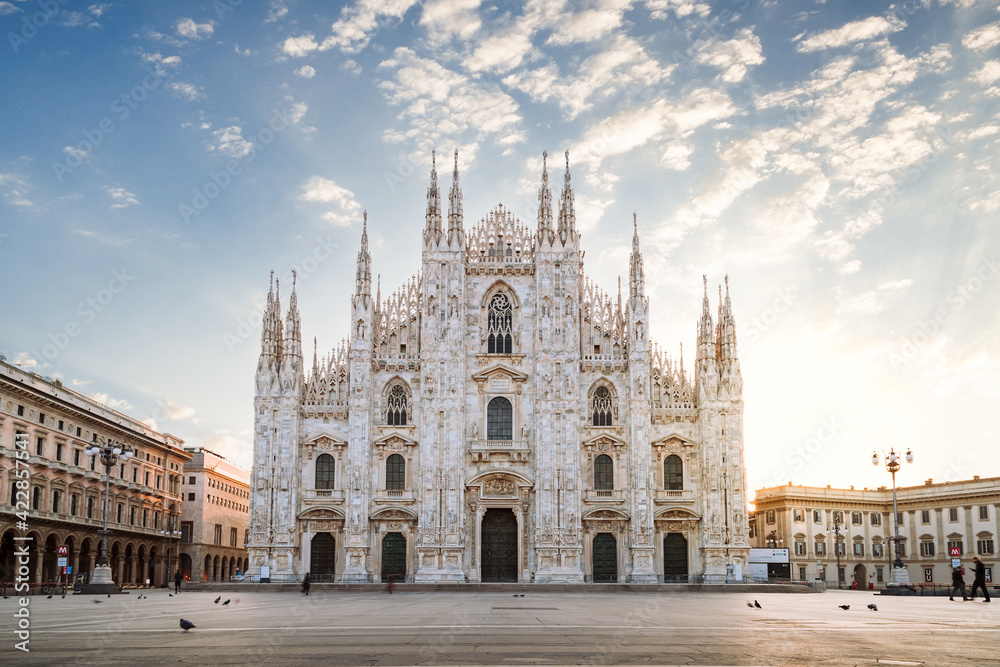 View of the Milan Cathedral with empty square due to the coronavirus blockade, with blue sky with white clouds and glow of light from the newly risen sun