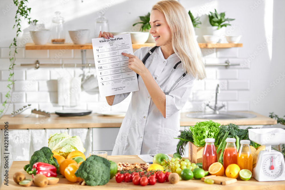 Smiling skilled confident nutritionist with meal plan and fresh healthy products on table