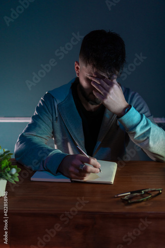 Young concentrated man writing a book in low light environment