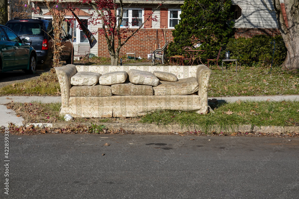 Old worn out couch by the curb waiting for trash pickup in front of an