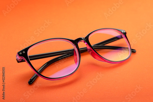 Glasses for vision, in a plastic frame, with transparent optics, on an orange sheet of paper, on a white background