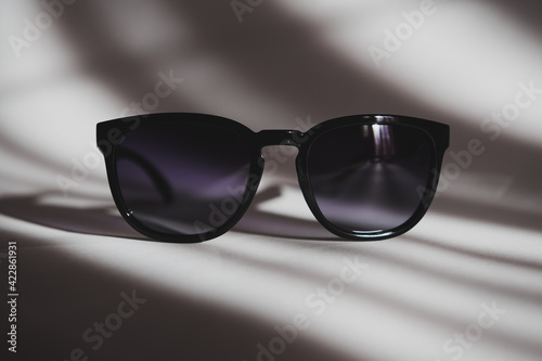 Stylish black sunglasses on the white background with shadows. Plastic glasses with gradient on a sunny day.
