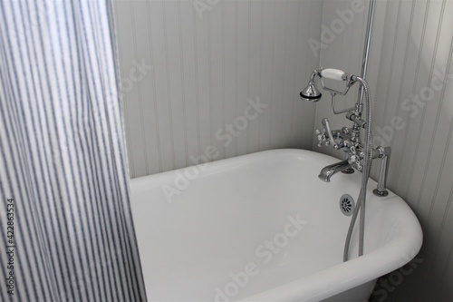 Bathtub tap for running water in a white clawfoot tub with a striped curtain. 