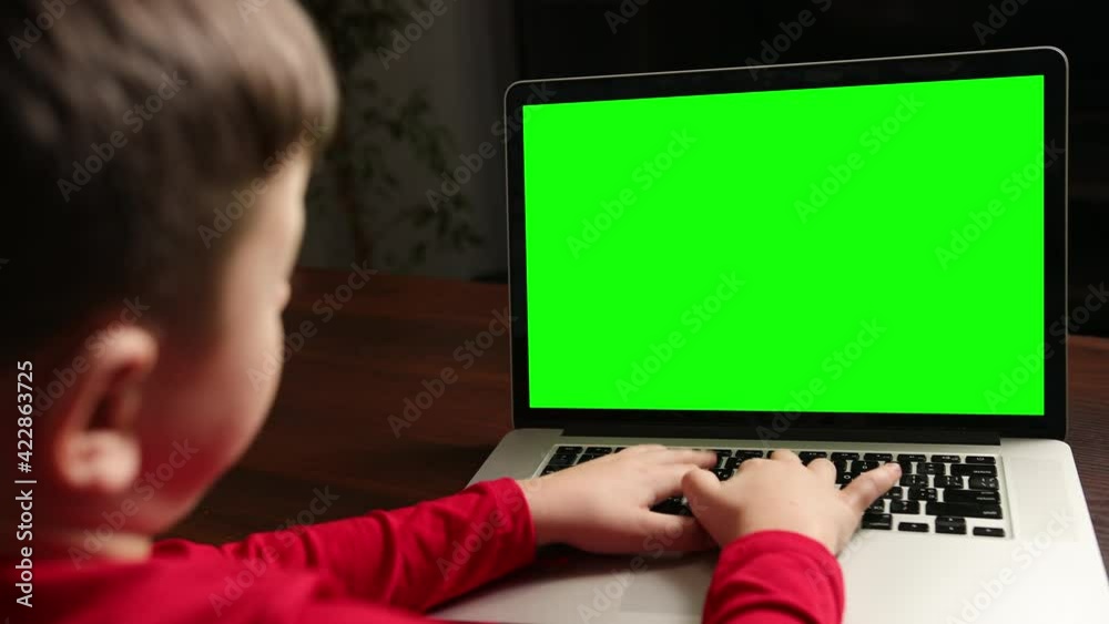 View from the back boy sitting at table typing on laptop with green chroma key View from the back boy sitting at table typing on laptop with green chroma key