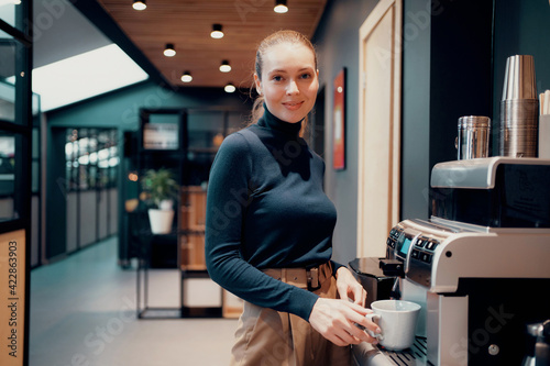 The coffee machine pours hot Americano coffee in the office. Business clothes, favorite work. Blue eyes, looking at the camera.