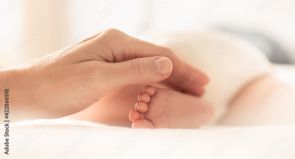 Child care love and support. Mothers hand touching teeny baby feet Child care love and support. Mothers hand touching teeny baby feet