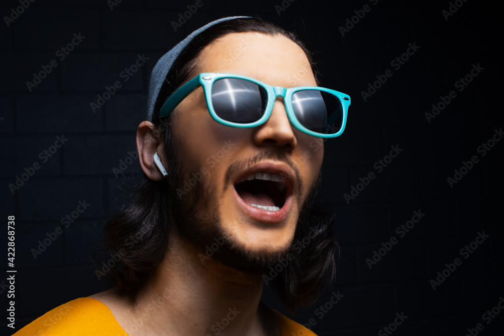 Studio portrait of young man with wireless earphones wearing blue sunglasses on black background. Studio portrait of young man with wireless earphones wearing blue sunglasses on black background.