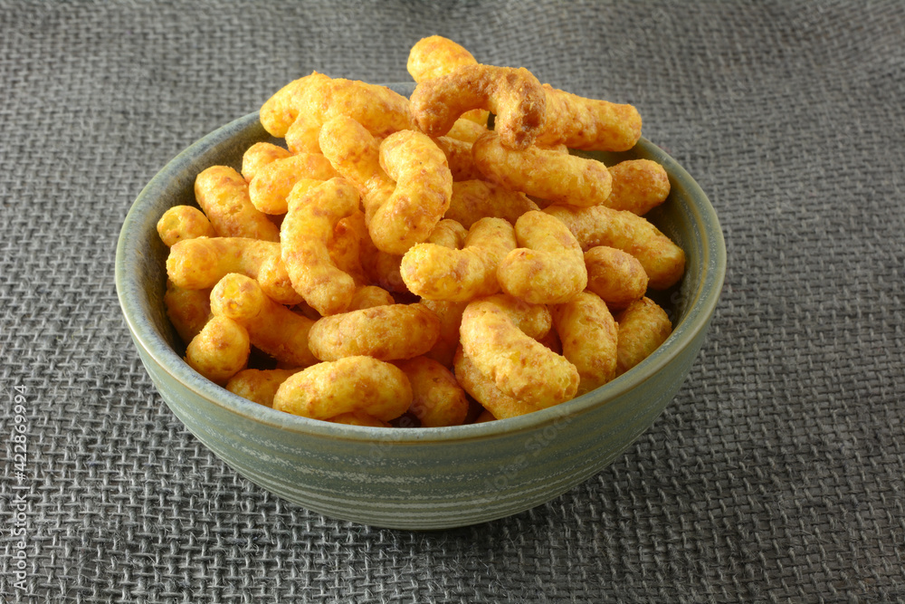 Peanut buttery corn puff snack in ceramic bowl on grey burlap Peanut buttery corn puff snack in ceramic bowl on grey burlap