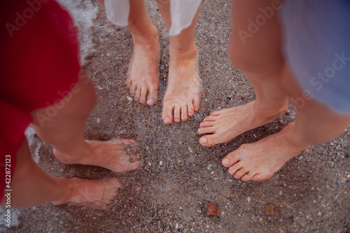bare feet of three girls stand on wet sand