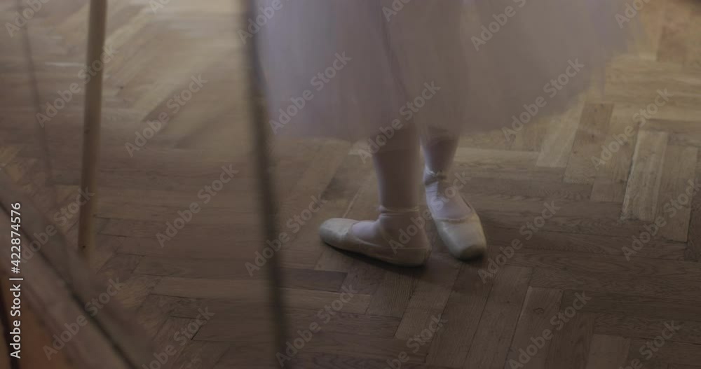Cinematic close up shot of an young graceful classical ballet female dancer feet in pointe shoes and white tutu is performing a choreography on classic theatre stage with dramatic lighting before sta