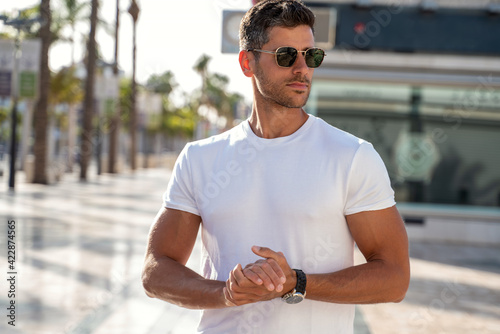 Billede på lærred Portrait of handsome young man wearing sunglasses and white tshirt, posing on city street background