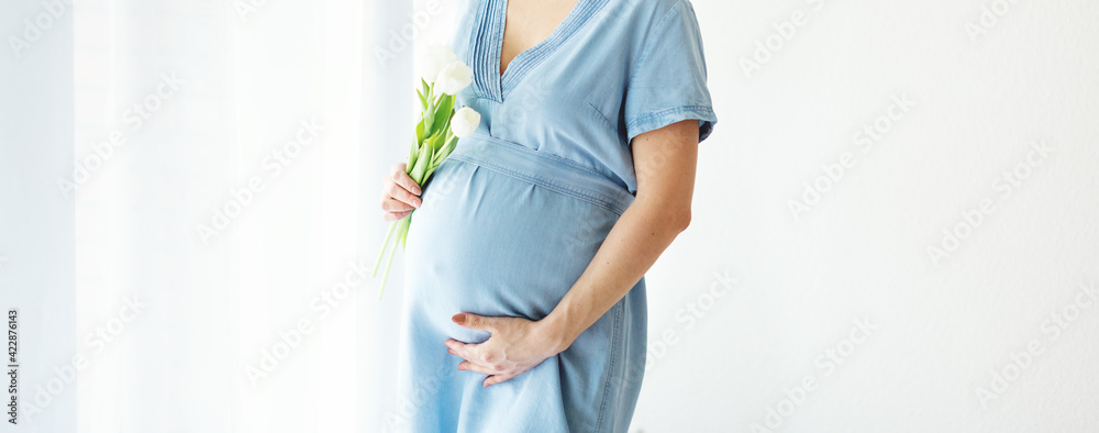 Pregnant woman holding spring flowers - obrazy, fototapety, plakaty 
