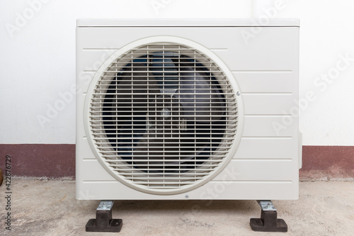 Condenser unit or compressor outside home or residential building. Unit of central air conditioner (AC) or heating ventilation air conditioning system (HVAC). Electric fan and refrigerant pump inside.