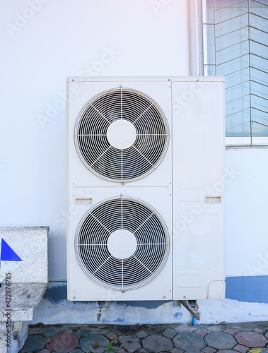 Condenser unit or compressor outside home or residential building. Unit of central air conditioner (AC) or heating ventilation air conditioning system (HVAC). Electric fan and refrigerant pump inside.