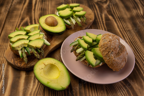 Healthy vegetarian organic breakfast meal, sandwich food made from asparagus, avocado, cucumber, soft cheese on whole grain buns. Wooden board, close up
