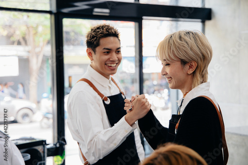 Cheerful young Asian man and woman hairdresser wearing apron uniform in modern salon giving high-five to each other on celebrating success of salon © twinsterphoto