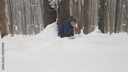 It is snowing heavily. Drunk caucasian man without jacket freezes in forest sitting on snow near tree. Concept of problems of homeless people and people who have harmful addictions to alcohol, drugs