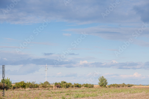 Transmission towers, pylons, power towers, adapted for high voltage electricity transportation and distribution, in front of unused fields in an agricultural background.